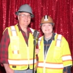 two adults in safety vests taking a photobooth photo in front of a microphone
